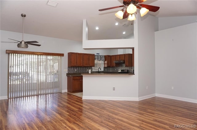 kitchen featuring sink, dark wood-type flooring, high vaulted ceiling, kitchen peninsula, and decorative backsplash