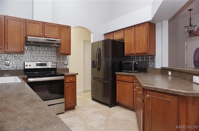 kitchen featuring backsplash, range hood, appliances with stainless steel finishes, decorative light fixtures, and a chandelier