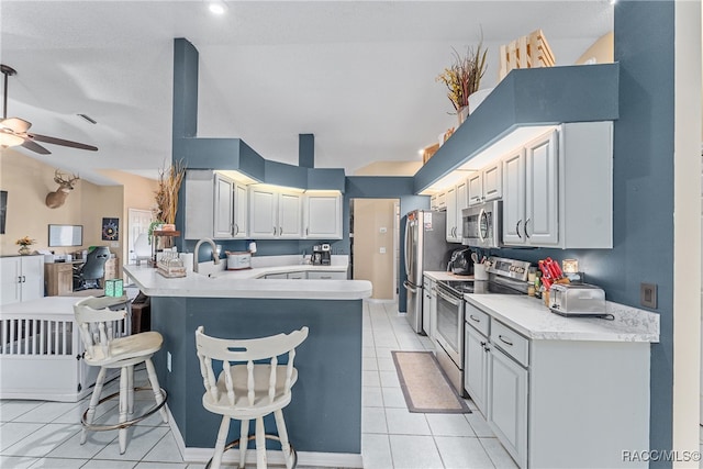 kitchen with kitchen peninsula, appliances with stainless steel finishes, light tile patterned floors, and a kitchen breakfast bar