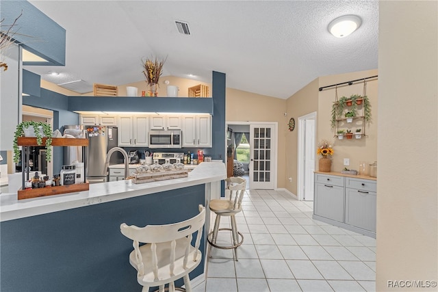 kitchen with lofted ceiling, white cabinets, a textured ceiling, appliances with stainless steel finishes, and a kitchen bar