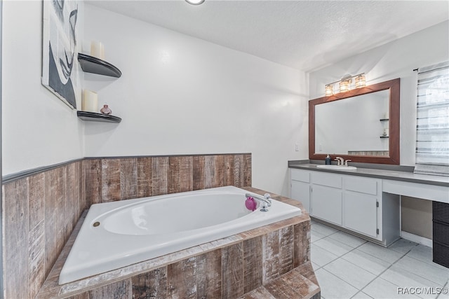 bathroom with tile patterned flooring, a relaxing tiled tub, a textured ceiling, and vanity