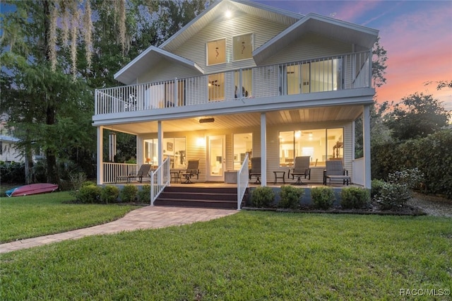 back house at dusk featuring covered porch and a yard