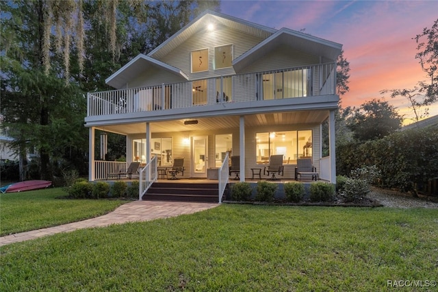 back house at dusk featuring a balcony, a yard, and covered porch