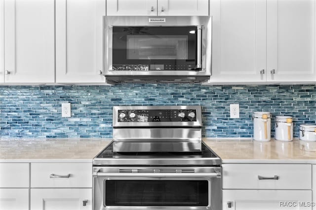 kitchen featuring decorative backsplash, white cabinetry, light stone counters, and appliances with stainless steel finishes