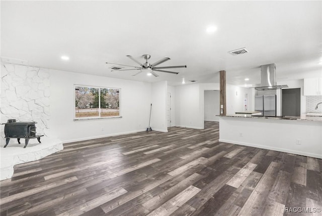 unfurnished living room with dark wood-type flooring, ceiling fan, and a wood stove