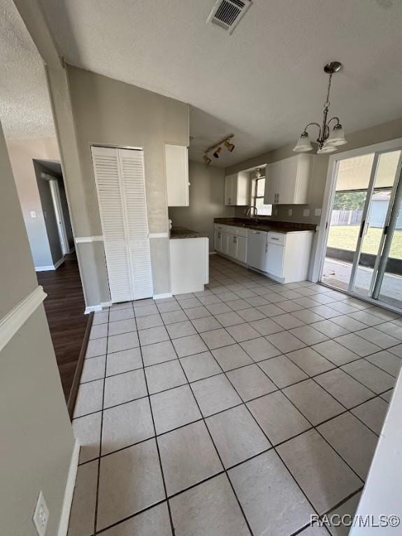 kitchen with light tile patterned floors, white cabinetry, hanging light fixtures, white dishwasher, and a chandelier