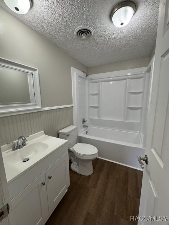 full bathroom with washtub / shower combination, hardwood / wood-style floors, vanity, a textured ceiling, and toilet