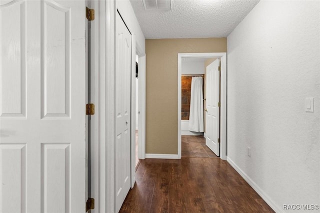 hall featuring dark wood-style flooring, a textured ceiling, baseboards, and visible vents