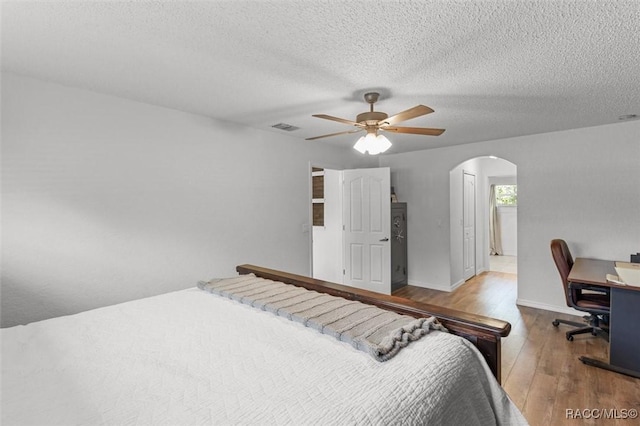 bedroom with baseboards, ceiling fan, visible vents, arched walkways, and hardwood / wood-style floors