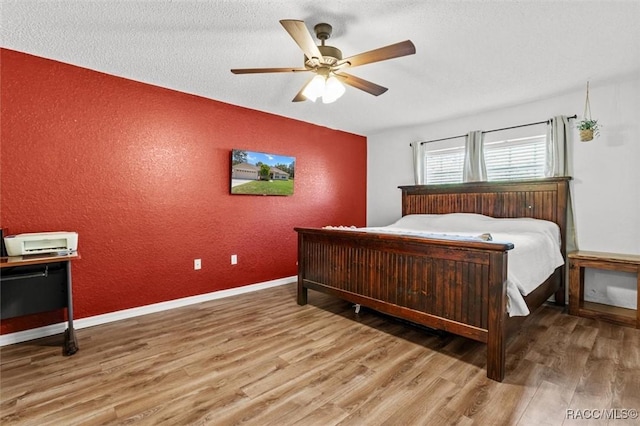 bedroom featuring a textured wall, wood finished floors, ceiling fan, and an accent wall