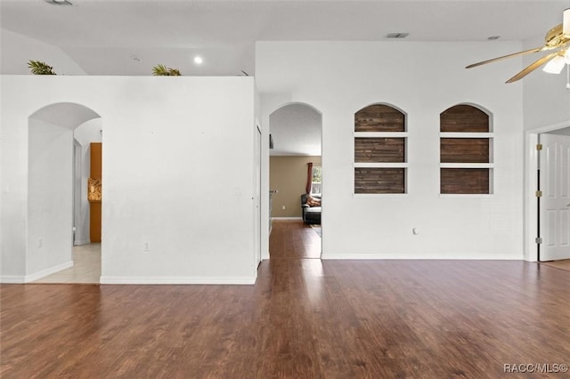 empty room with a ceiling fan, built in shelves, visible vents, and arched walkways