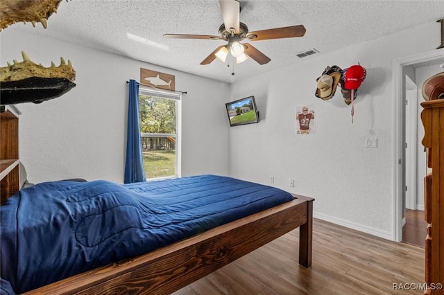 bedroom featuring wood finished floors, a ceiling fan, a textured ceiling, visible vents, and baseboards