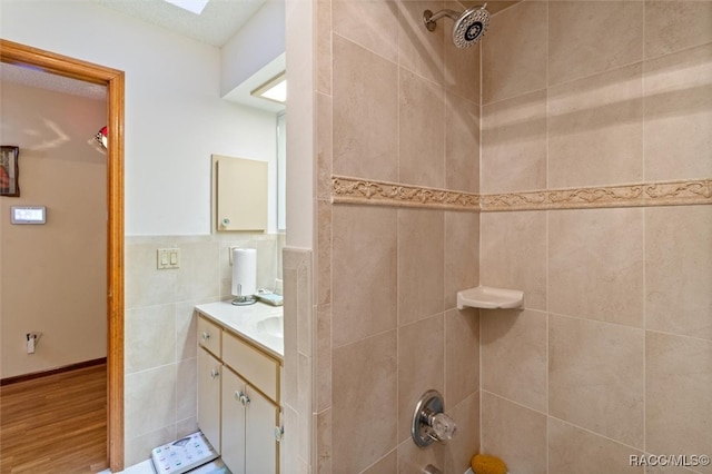 bathroom with vanity, hardwood / wood-style flooring, tiled shower / bath combo, and tile walls