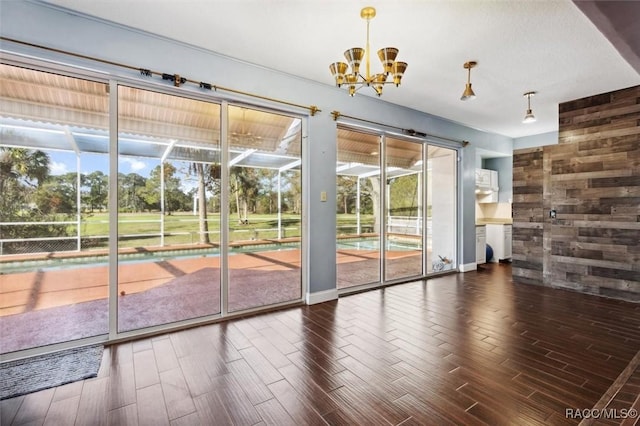 doorway with a sunroom, a notable chandelier, wooden walls, and wood finished floors