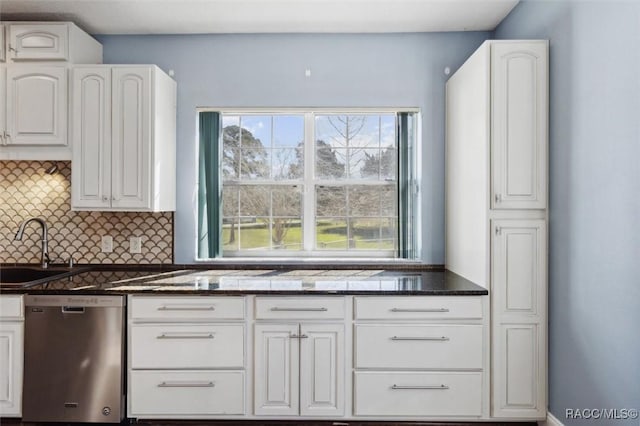 kitchen featuring dark stone counters, white cabinets, backsplash, stainless steel dishwasher, and a sink