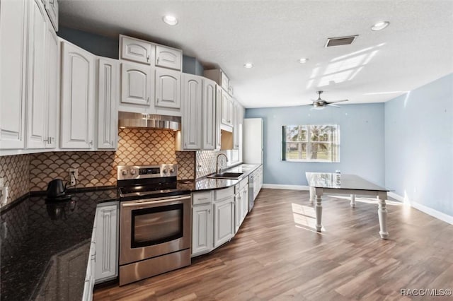 kitchen with visible vents, backsplash, a sink, wall chimney range hood, and stainless steel range with electric stovetop