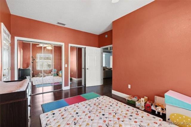 bedroom with wood finished floors, visible vents, baseboards, and two closets