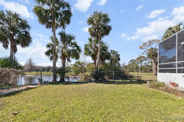 view of yard featuring a water view, glass enclosure, and fence