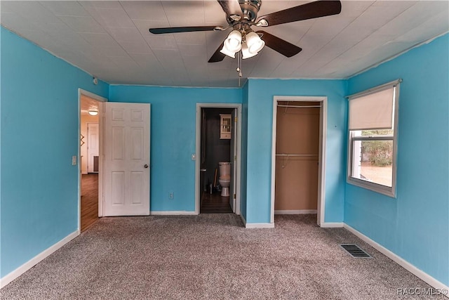 unfurnished bedroom featuring ensuite bathroom, a walk in closet, ceiling fan, a closet, and carpet flooring