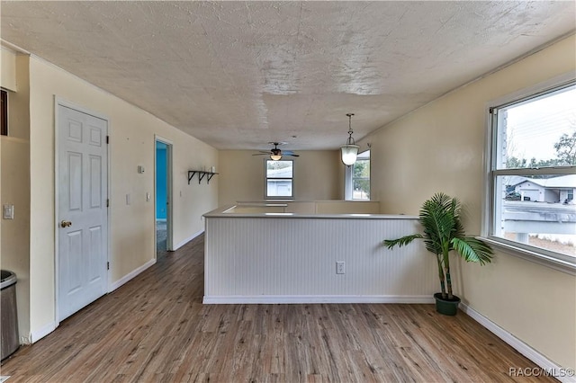 kitchen with a textured ceiling, kitchen peninsula, pendant lighting, and hardwood / wood-style flooring