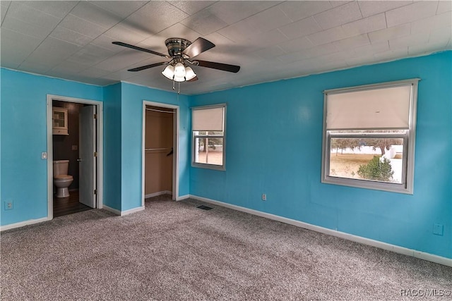 unfurnished bedroom featuring ceiling fan, carpet, ensuite bath, a closet, and a walk in closet