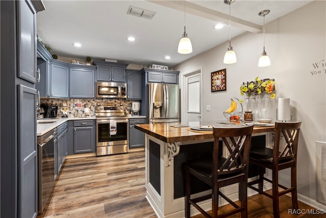 kitchen featuring stainless steel appliances, butcher block countertops, backsplash, hardwood / wood-style floors, and decorative light fixtures