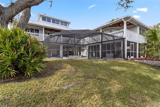 rear view of property featuring ceiling fan, glass enclosure, a balcony, and a yard