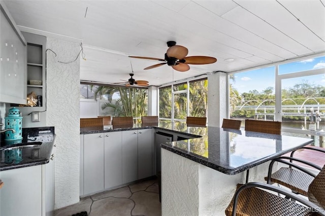 exterior space with dark stone counters, sink, gray cabinets, a water view, and ceiling fan