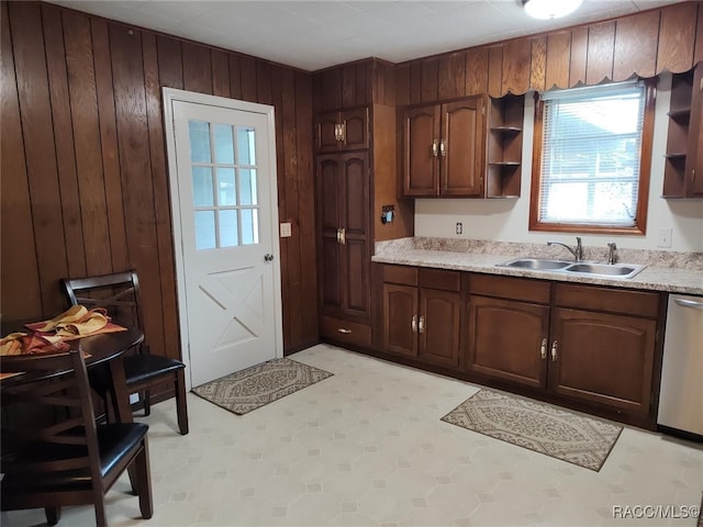 kitchen featuring dishwasher, dark brown cabinetry, wood walls, and sink