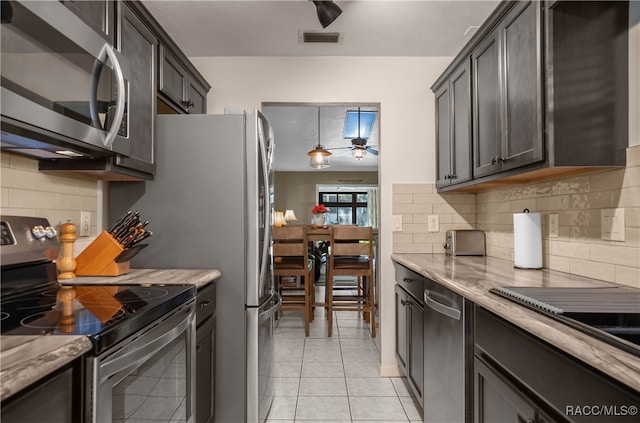 kitchen featuring dark brown cabinetry, hanging light fixtures, stainless steel appliances, light stone counters, and light tile patterned floors