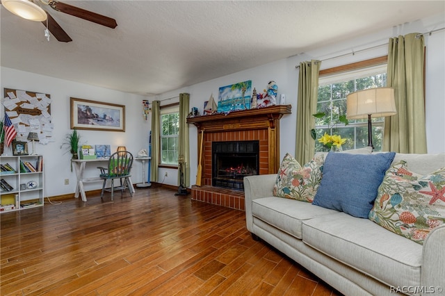 living room featuring a wealth of natural light, wood-type flooring, a textured ceiling, and a brick fireplace