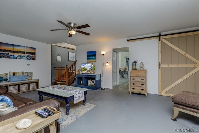 living room with ceiling fan, a barn door, a textured ceiling, and concrete floors