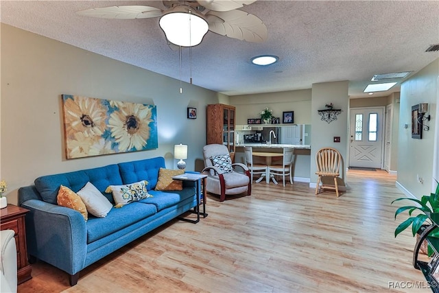 living room with light wood finished floors, visible vents, baseboards, and a textured ceiling