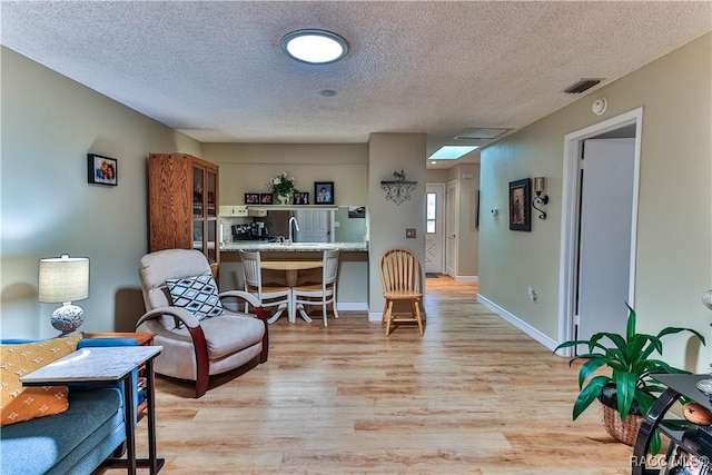 sitting room with baseboards, a textured ceiling, visible vents, and light wood-style floors