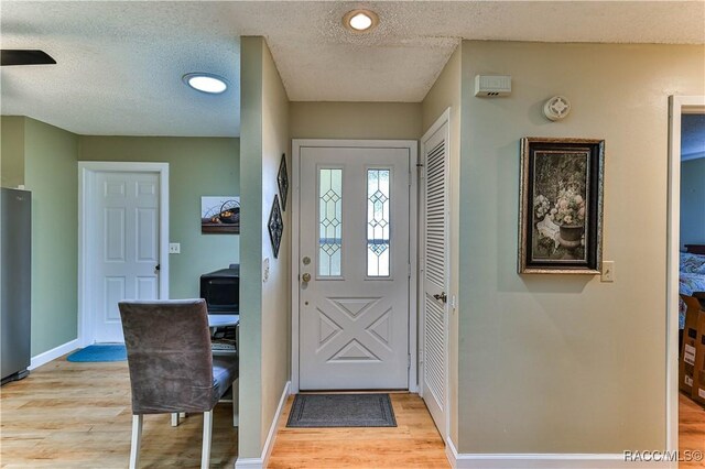 entrance foyer with a textured ceiling, light wood-style flooring, and baseboards