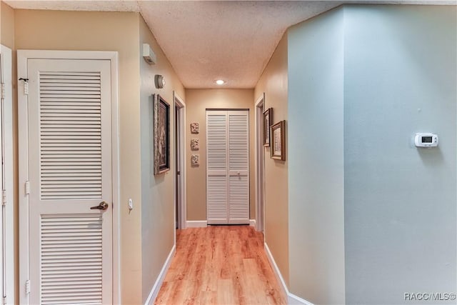 hallway with light wood-type flooring, a textured ceiling, and baseboards