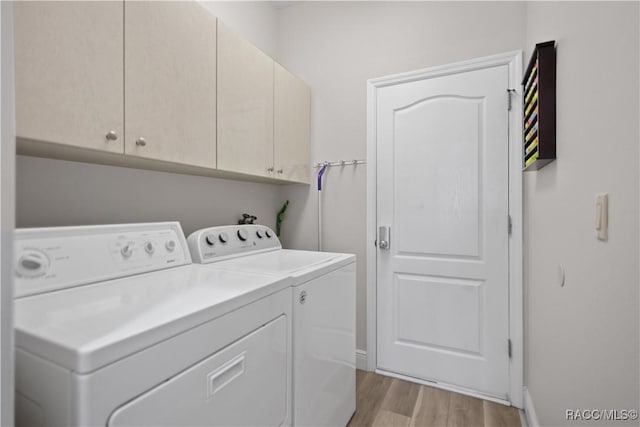 clothes washing area featuring cabinet space, washing machine and dryer, baseboards, and light wood-style flooring