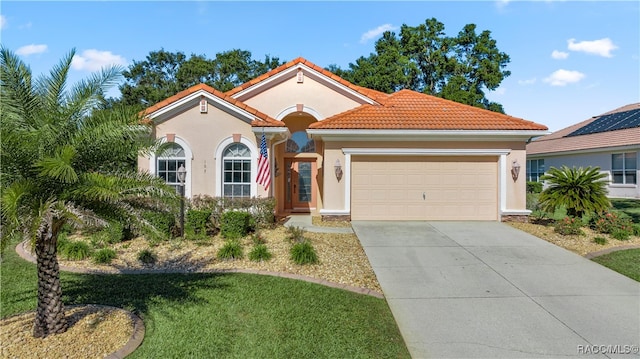 mediterranean / spanish home featuring a garage, a tiled roof, driveway, stucco siding, and a front lawn