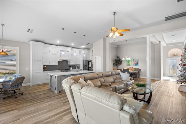 living room featuring sink, decorative columns, ceiling fan, and light wood-type flooring