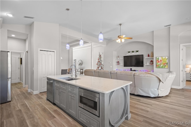 kitchen with sink, appliances with stainless steel finishes, a kitchen island with sink, hanging light fixtures, and gray cabinetry