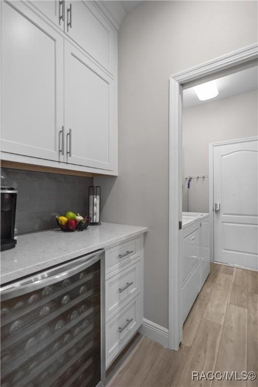 bar featuring white cabinetry, washer and dryer, beverage cooler, and light hardwood / wood-style floors