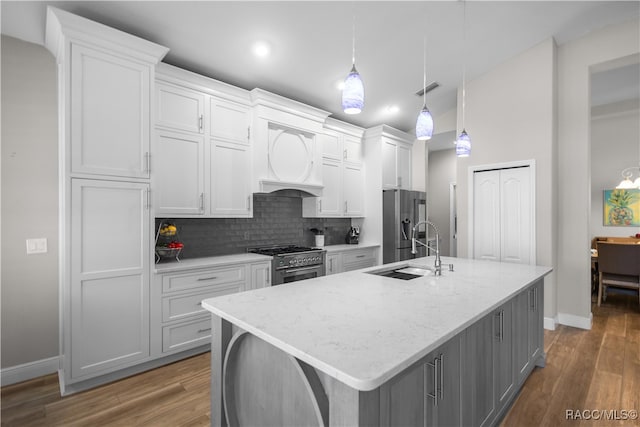 kitchen with decorative backsplash, appliances with stainless steel finishes, a kitchen island with sink, white cabinets, and a sink