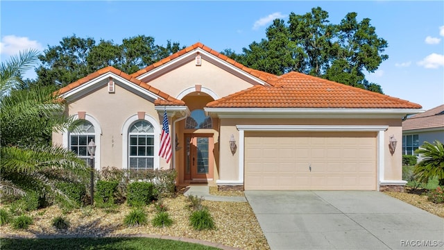 mediterranean / spanish home with an attached garage, a tiled roof, concrete driveway, and stucco siding