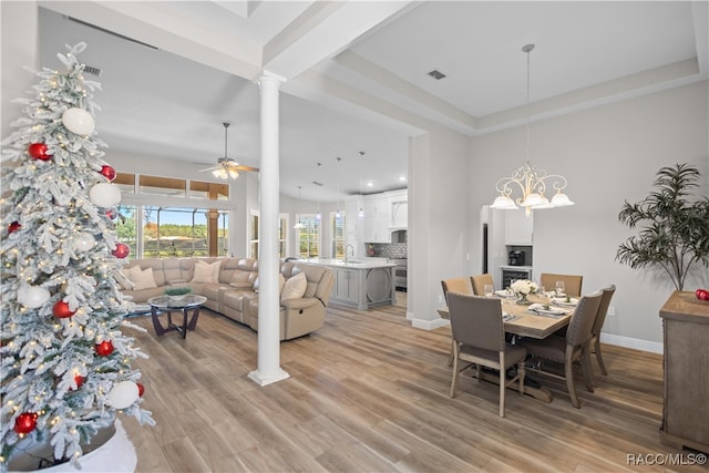 dining area with light wood-style floors, baseboards, ornate columns, and ceiling fan with notable chandelier