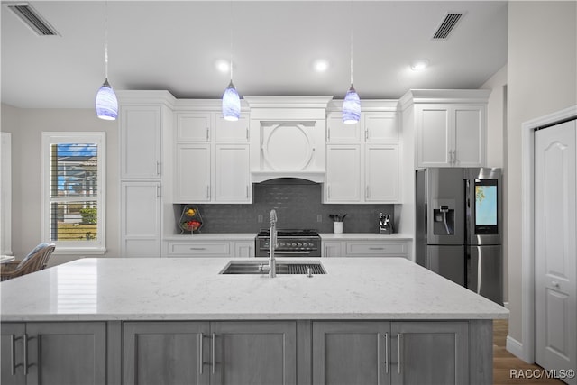 kitchen featuring stainless steel appliances, premium range hood, an island with sink, and visible vents