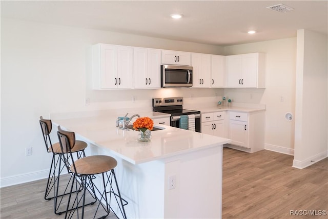 kitchen with white cabinetry, a breakfast bar, kitchen peninsula, and appliances with stainless steel finishes