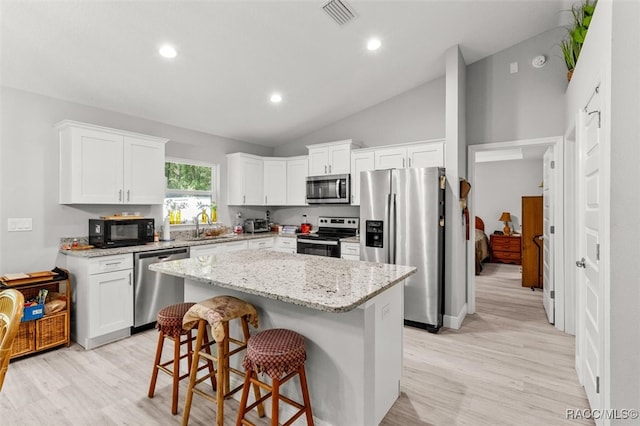 kitchen with light stone counters, stainless steel appliances, vaulted ceiling, white cabinets, and a center island