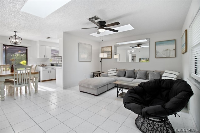 tiled living room with a textured ceiling, ceiling fan with notable chandelier, and a skylight