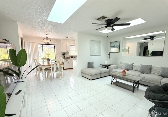 living room with a textured ceiling, a skylight, light tile patterned flooring, and ceiling fan with notable chandelier