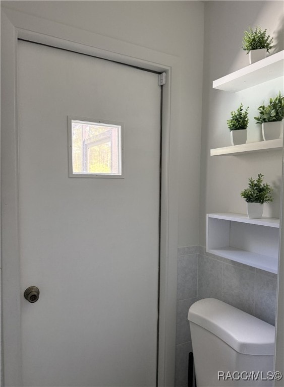 bathroom with toilet and tile walls